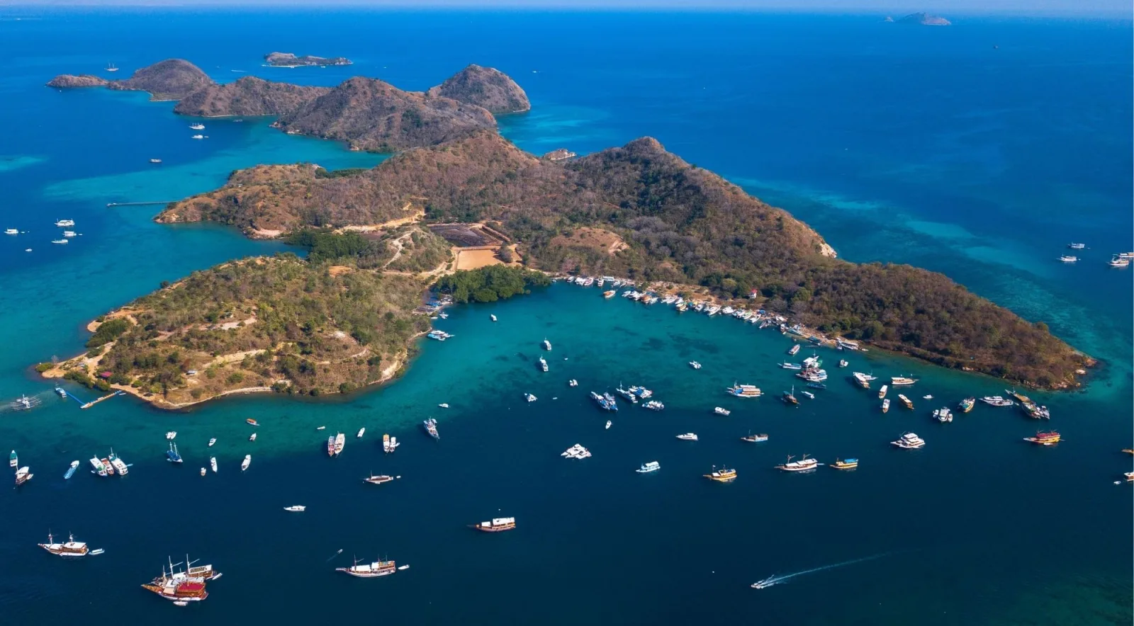 Aerial view of a green island ringed by reef with boats scattered across deep blue water