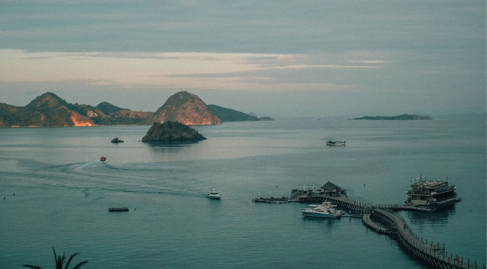 A small island and a long wooden jetty in flat pale water under an overcast sky