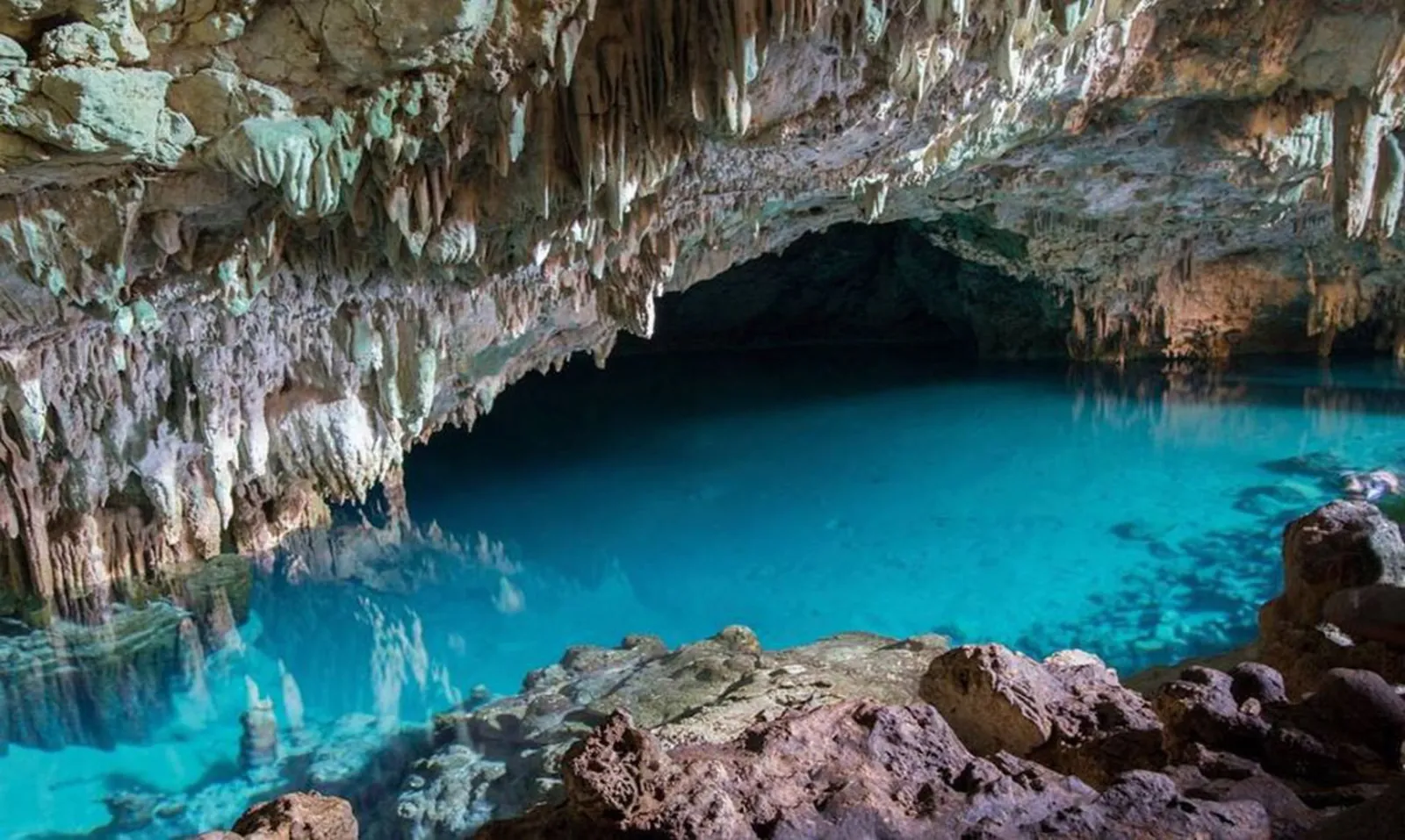 Stalactites hanging over the saltwater pool inside Rangko Cave
