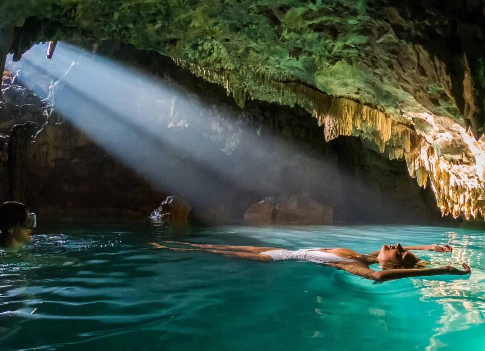 A swimmer in the shaft of daylight falling into the Rangko Cave pool