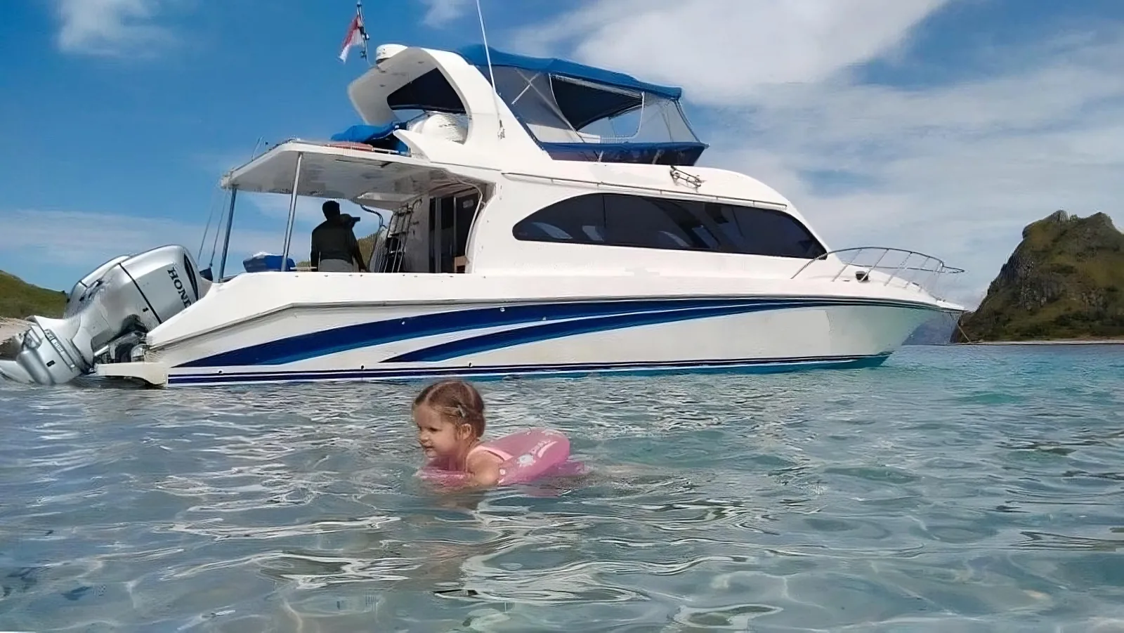 Child swimming in shallow clear water beside the tour speedboat