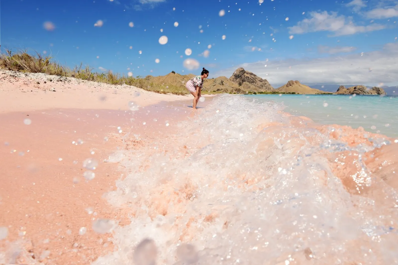 Close-up of the pink sand at Pantai Merah with a visitor walking the shoreline