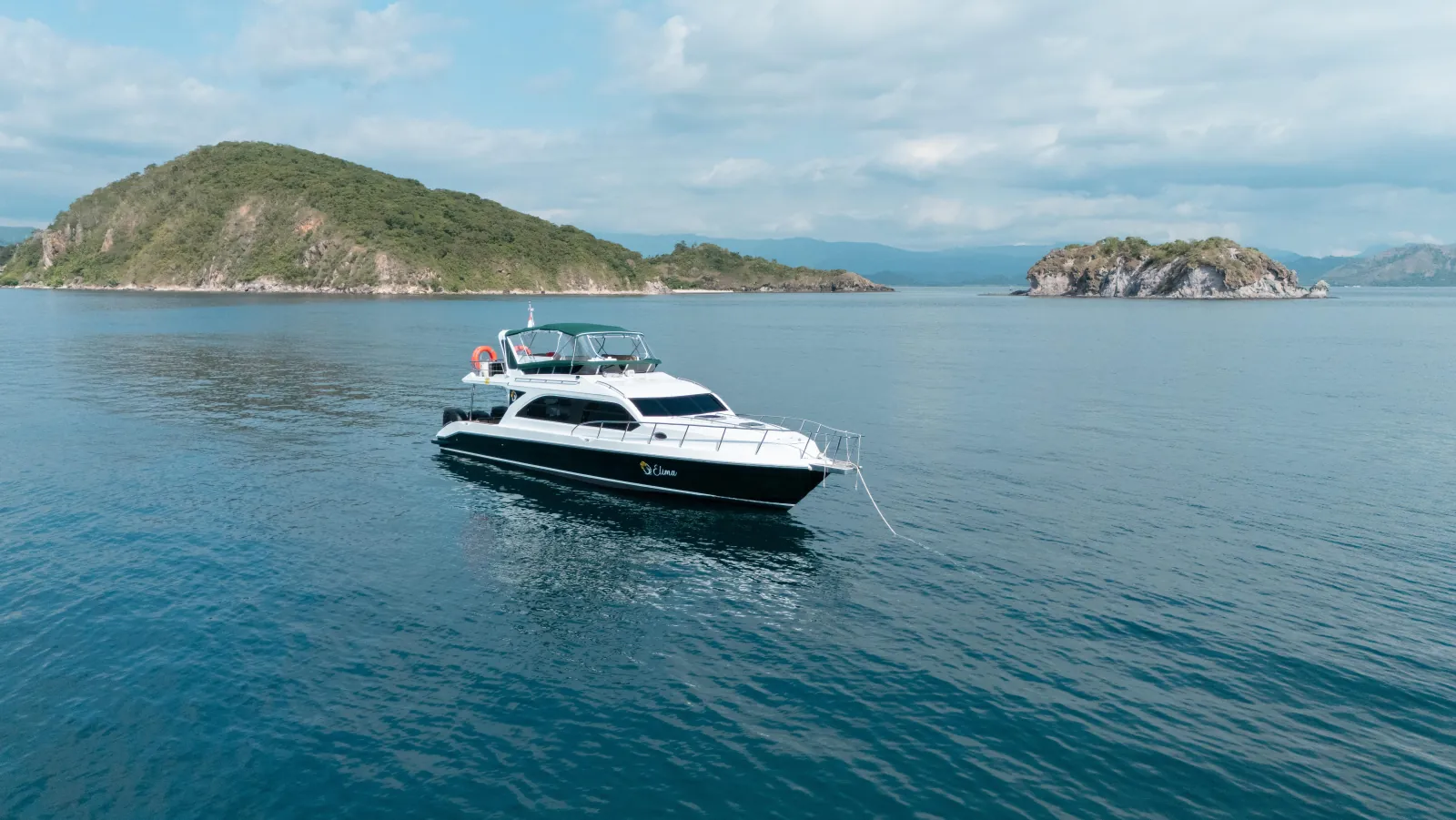 White speedboat at anchor on flat blue water off a green Komodo island