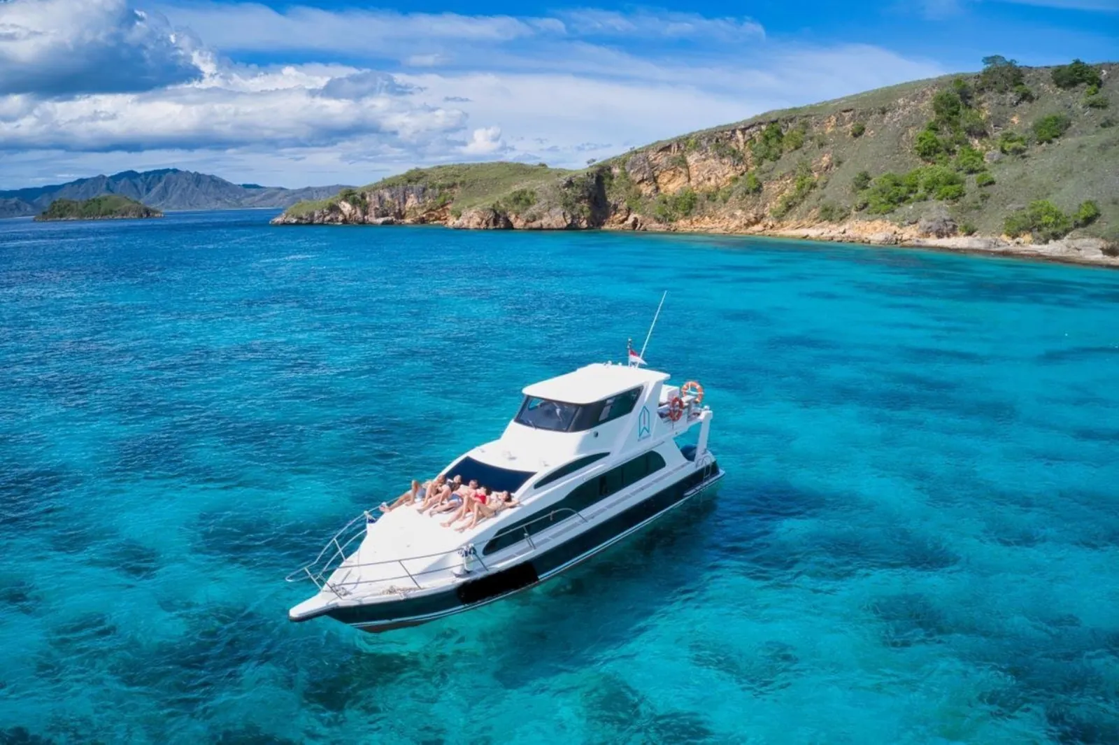 Shared tour speedboat moored over shallow reef beside a green island